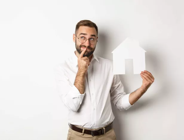 real-estate-man-thinking-while-searching-for-apartment-holding-paper-house-model-standing-compressed